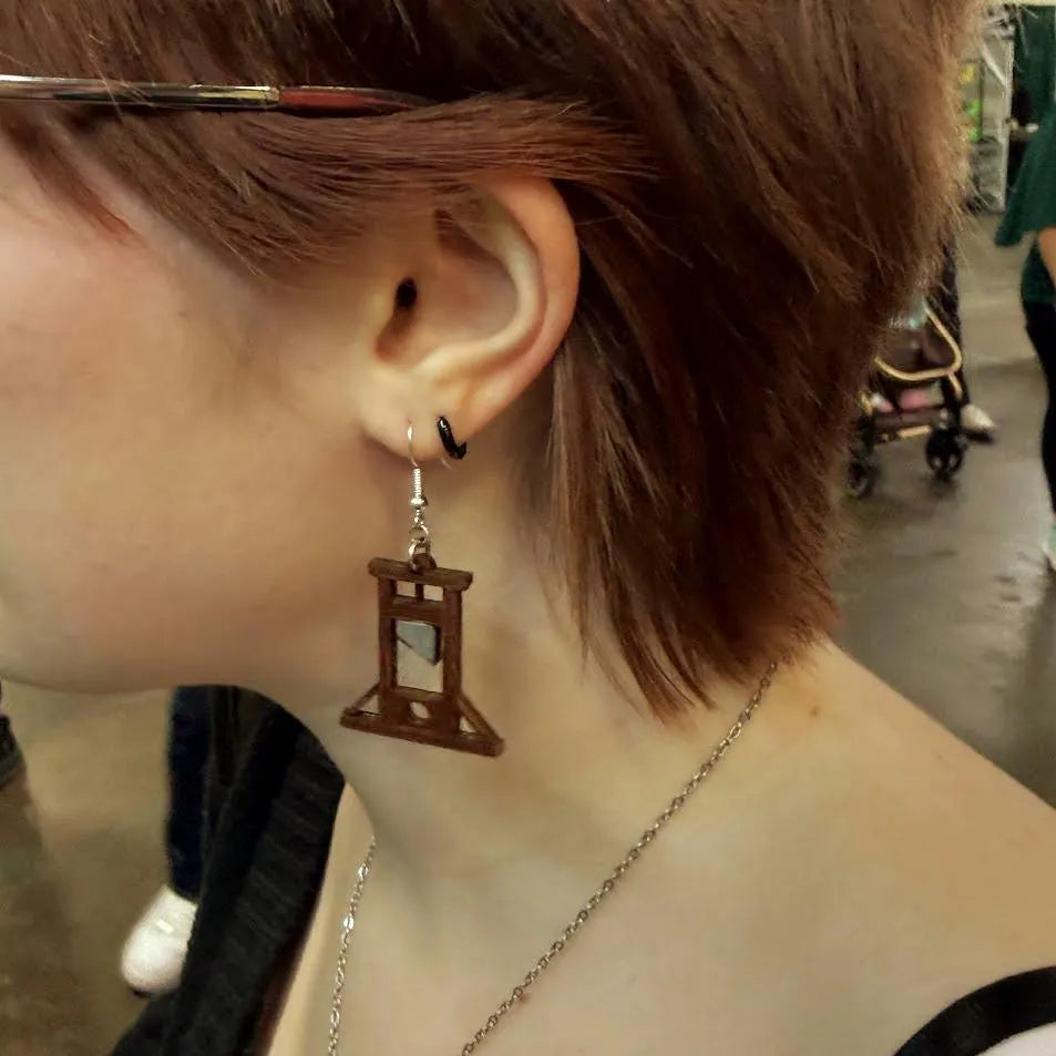 Close-up of hand-painted wooden guillotine dangle earrings with hypoallergenic sterling silver hooks, lightweight gothic history jewelry by Cate’s Concepts.
