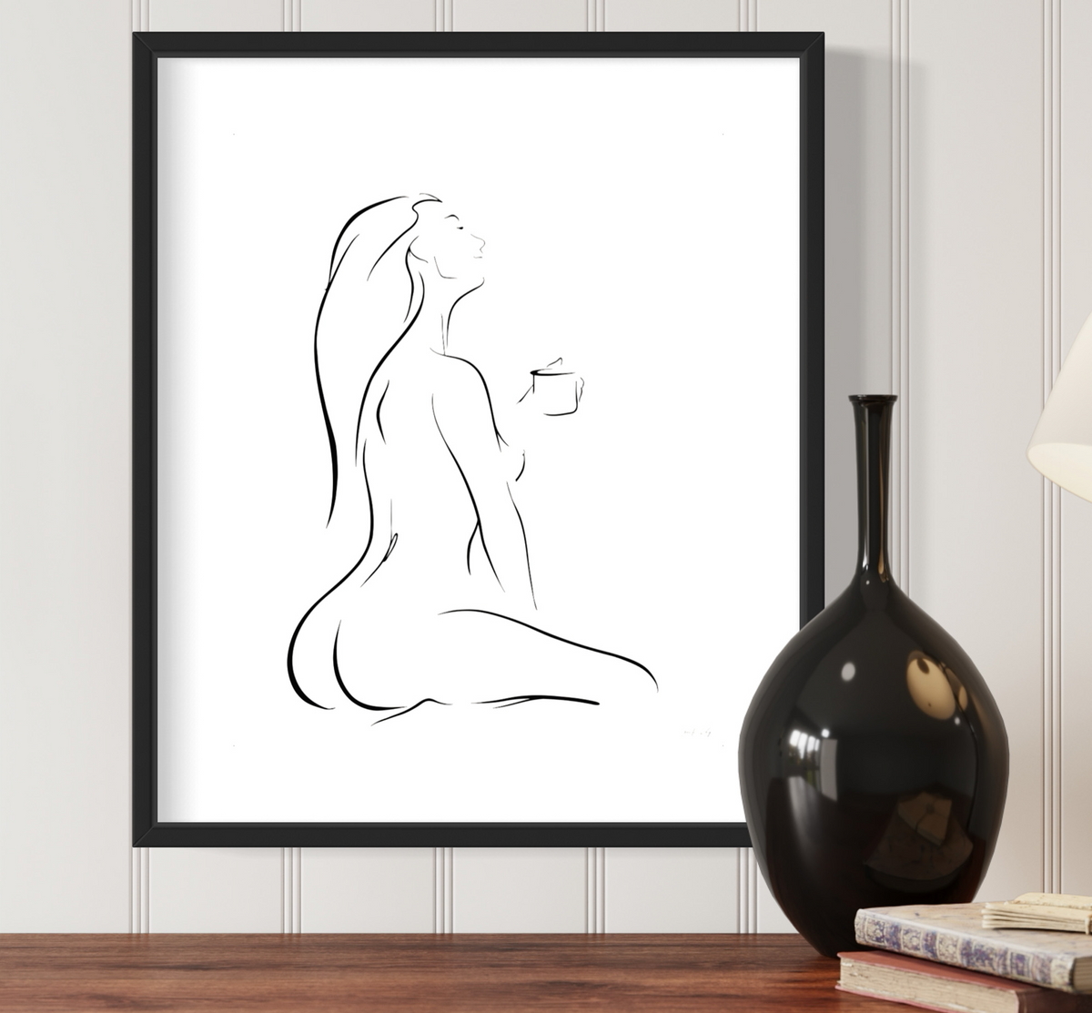 Black and white elegant line art illustration of a sensual woman enjoying her first cup of coffee, head tilted back, in a peaceful pose, titled "But First, Coffee"; black frame on white wainscoting with modern black decor
