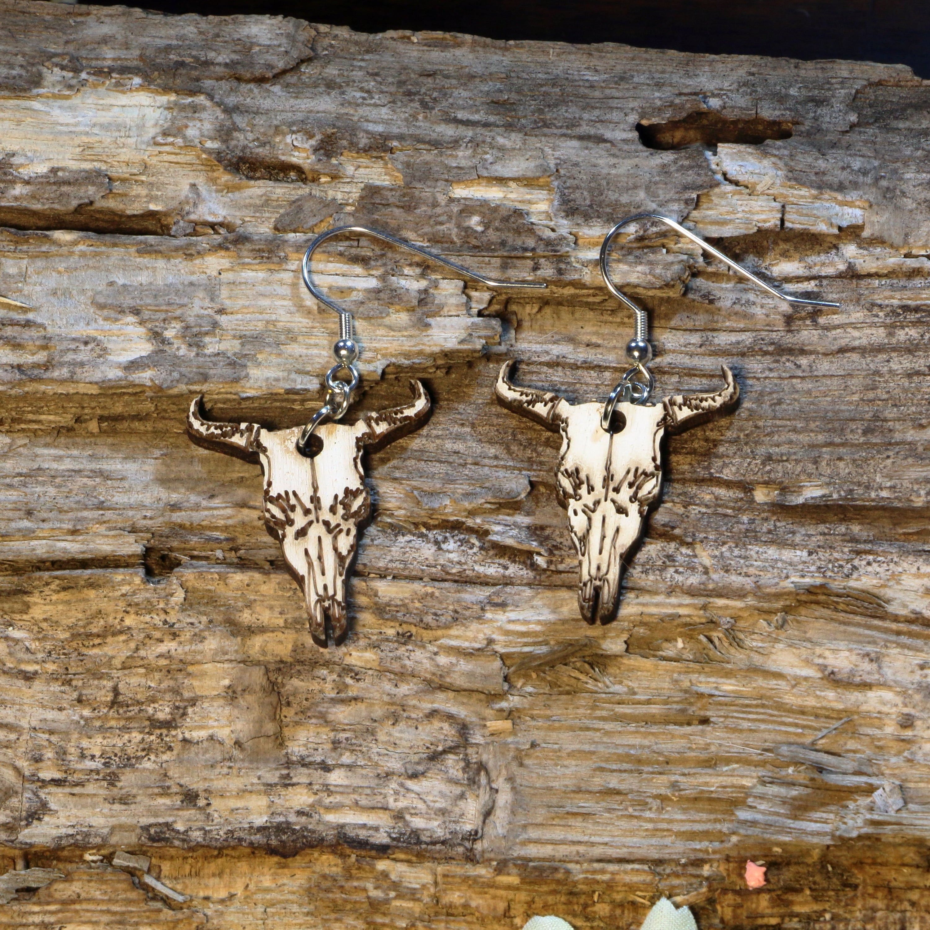 Hand-painted wooden longhorn cattle skull dangle earrings featuring a detailed western cow skull with curved horns inspired by the American Southwest. Crafted from lightweight wood with hypoallergenic .925 sterling silver hooks, these rustic earrings are perfect for western fashion, rodeo fans, ranch life, cowgirl style, country music festivals, Texas pride, and anyone who loves southwestern-inspired jewelry.