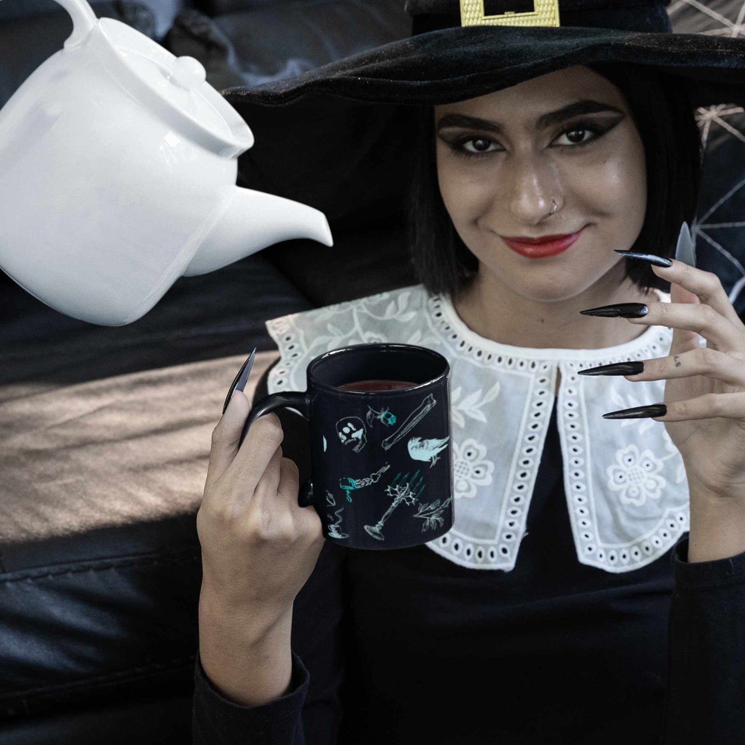 Person in a witch hat holding a cybergoth Victorian zombie icons mug while a white teapot pours
