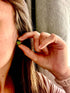 A close-up lifestyle shot of a woman wearing a small green beaded earring, holding her hand near her ear to show the earring&