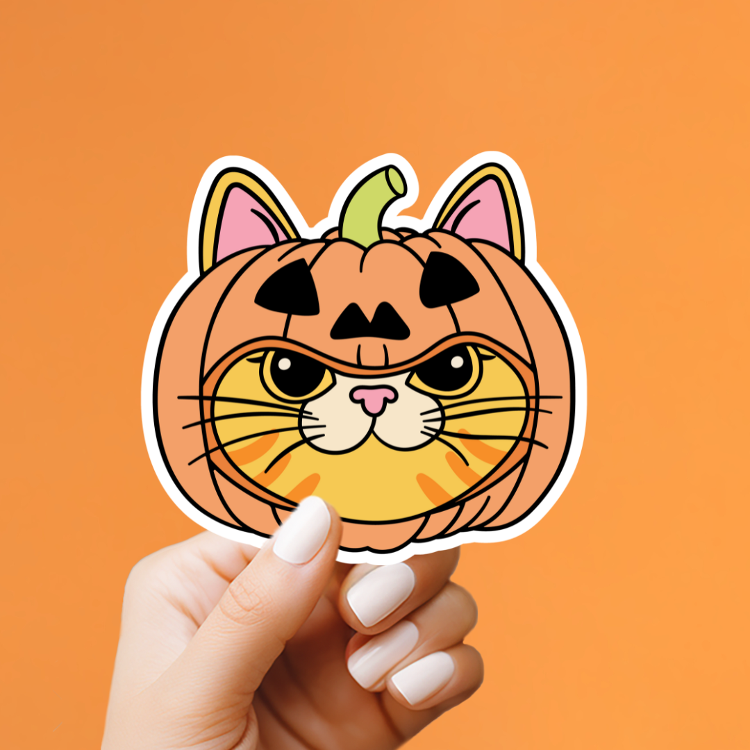 A hand with white manicured nails holds a die-cut sticker shaped like a pumpkin cat face with a grumpy expression, set against a solid orange background.