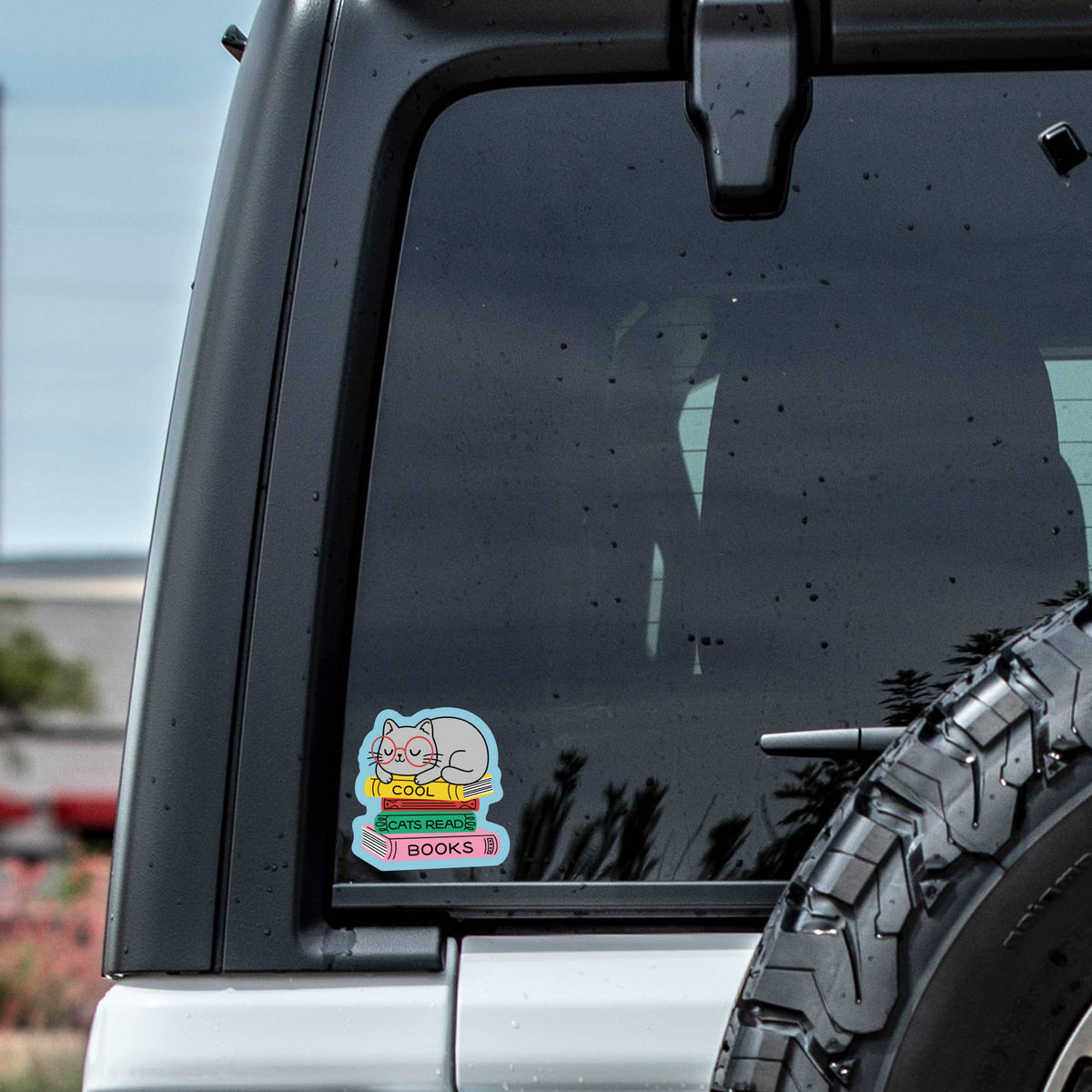 Car window with a sticker featuring a cartoon character and text, outdoors.