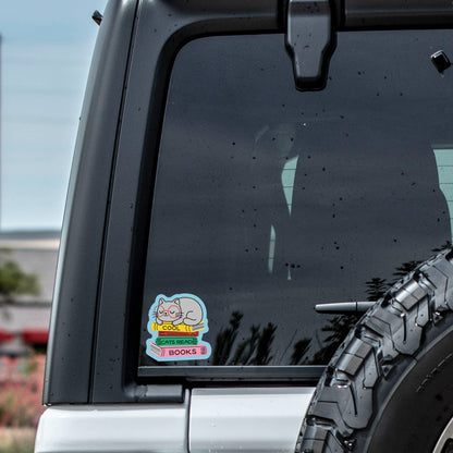 Car window with a sticker featuring a cartoon character and text, outdoors.