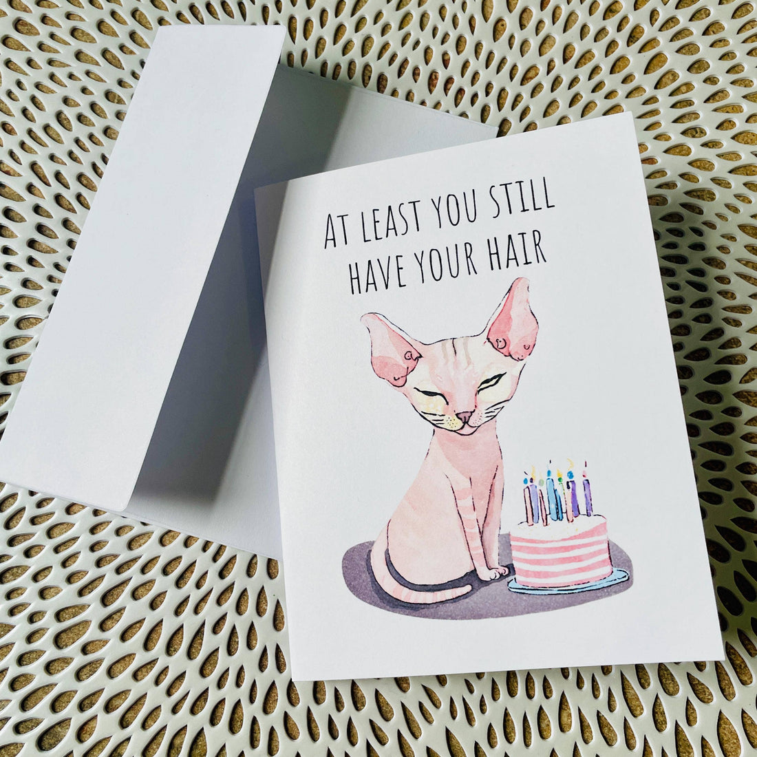 Greeting card with a cat and birthday cake illustration on a textured surface