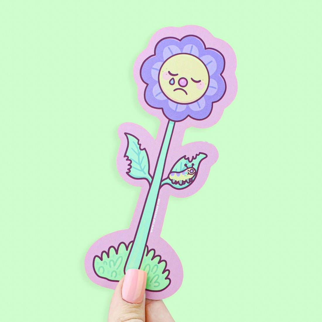 Sticker of a flower with a sad face held against a light green background