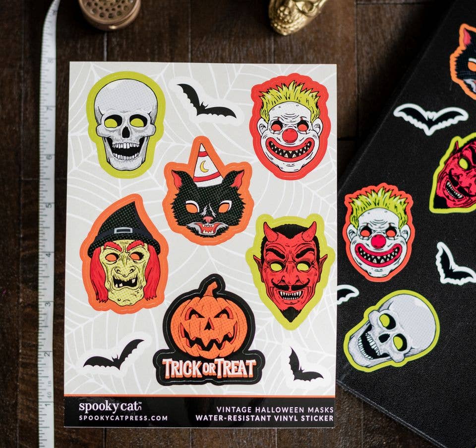 A sheet of vintage-style Halloween vinyl stickers displayed on a dark wooden surface next to a ruler and a black sticker roll. The stickers feature classic spooky faces and motifs including a skull, clown, witch, devil, cat in a hat, jack-o&