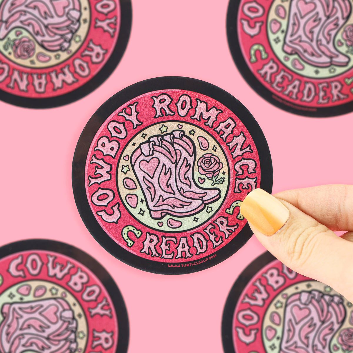 A hand with yellow nails holds a round sticker featuring a pink cowboy boot and the words &