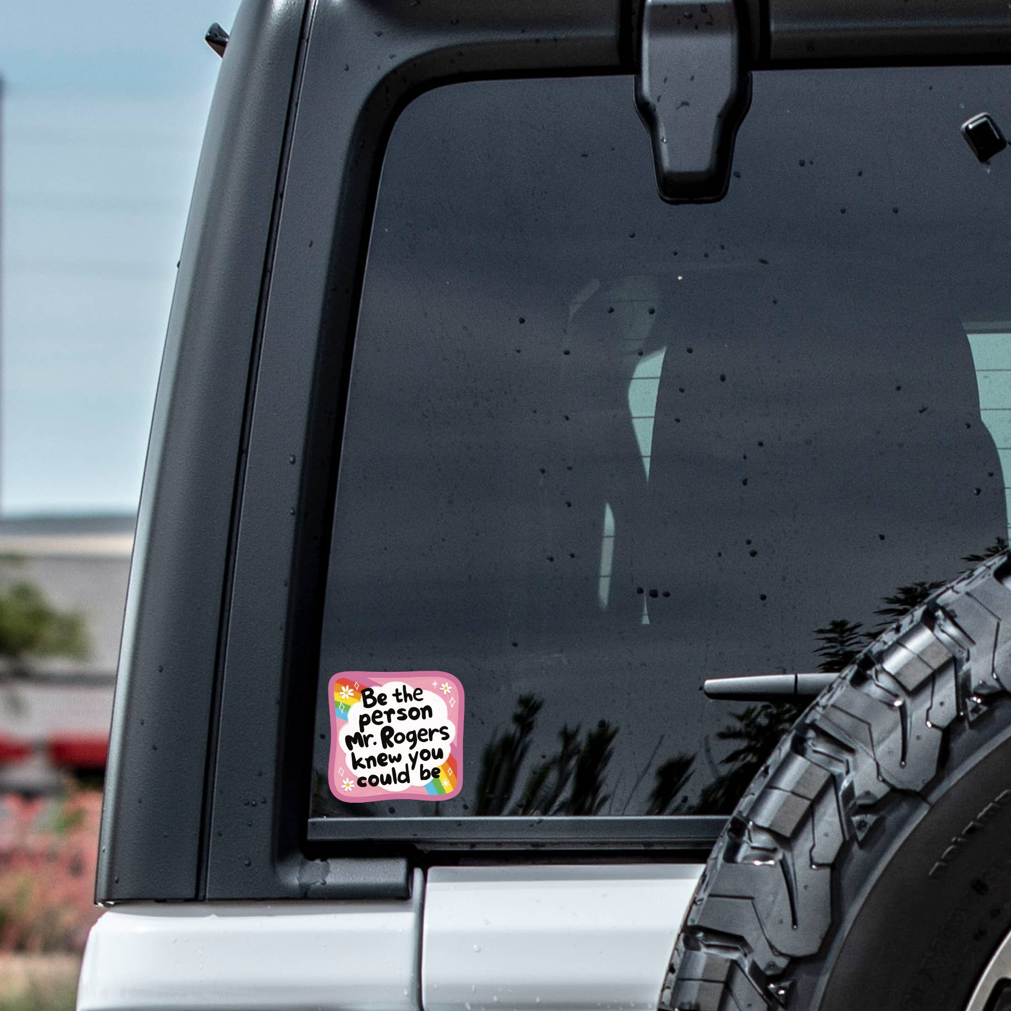 Car window with a sticker featuring text and graphics, outdoors.