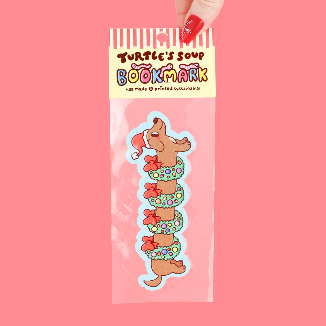 Bookmark with holiday themed weenie dog design in clear packaging on a pink background