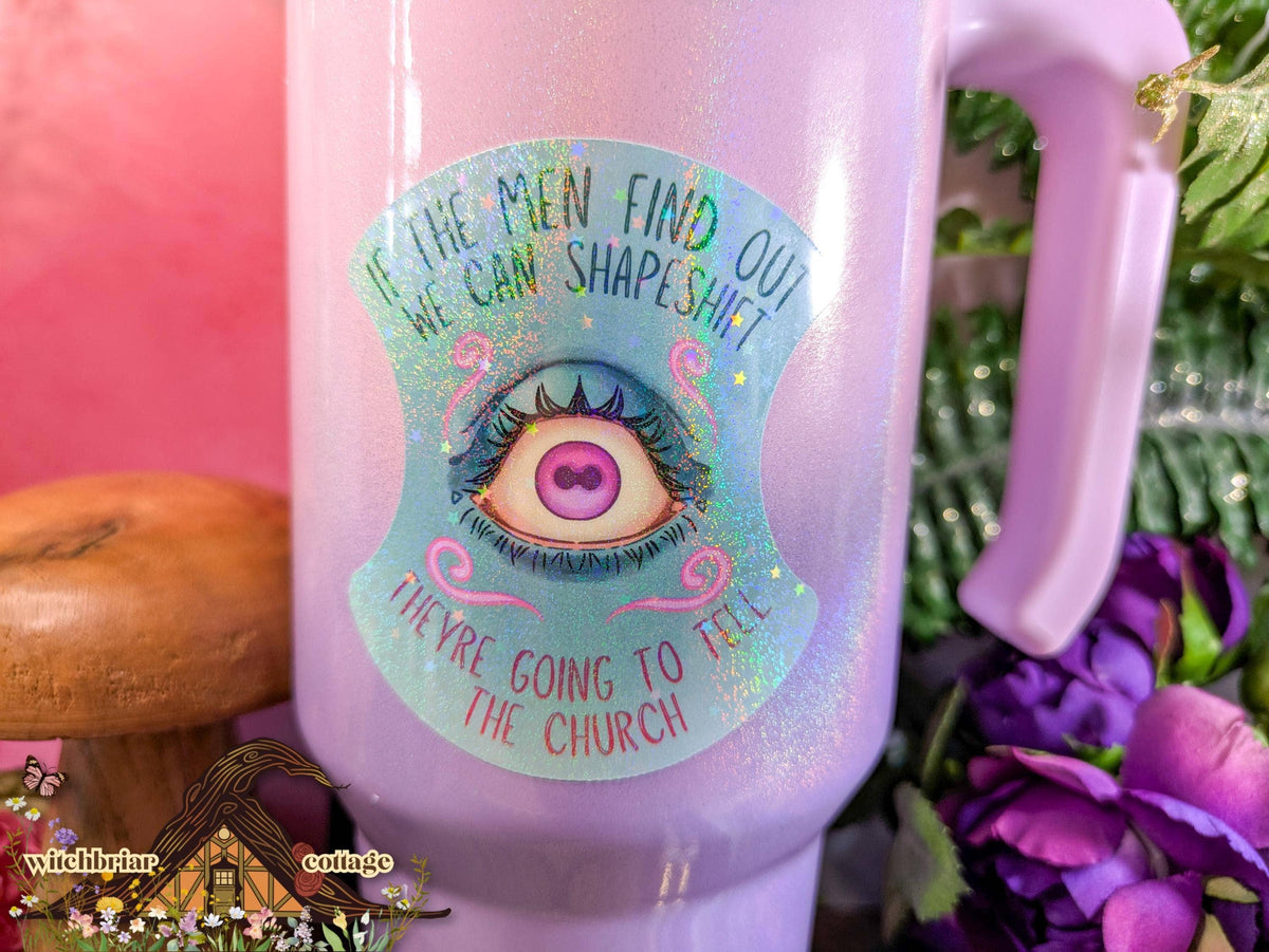 Pink mug with a colorful label featuring an eye design and text, surrounded by flowers and a pink background.