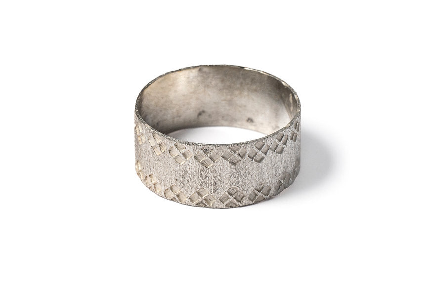 A textured sterling silver cigar band ring with a handstamped diamond design on the edging, made ethically in. mexico of recycled metals, flat lay