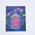 A folded greeting card with a vibrant blue background, featuring a bottle of &