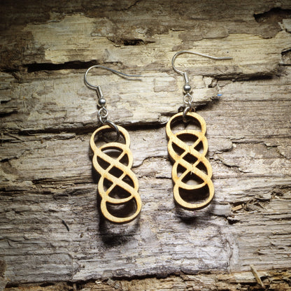 Pair of natural wood double infinity symbol dangle earrings with interlocking geometric loops displayed on rustic weathered wood