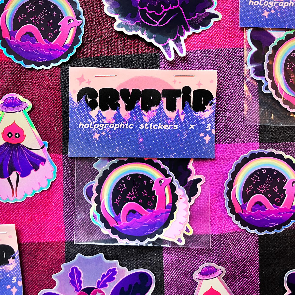 A set of colorful holographic stickers featuring a purple snake in a starry night sky under a rainbow, displayed on a pink and black checkered background. A central card reads &