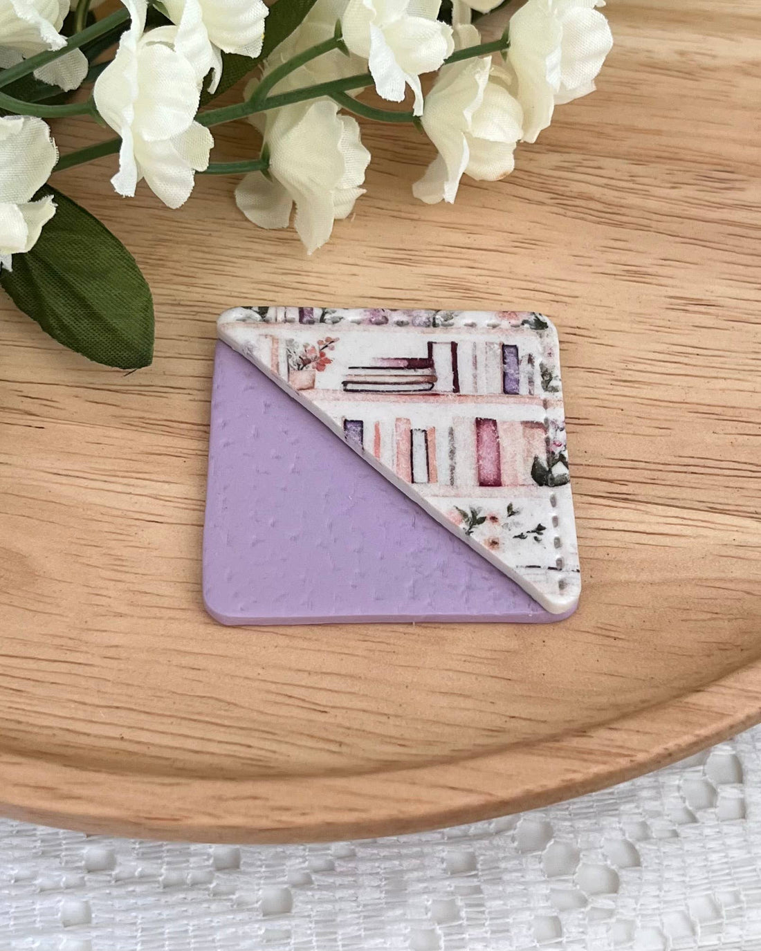 Floral-patterned and purple corner bookmark on a wooden surface with white flowers in the background.