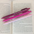Two pink pens with text on them lying on an open book