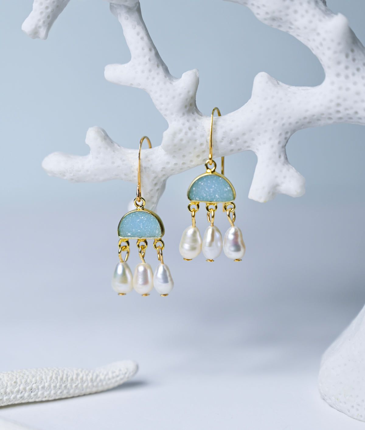 Close up view of blue chalcedony and pearl chandelier earrings hanging from a coral branch.