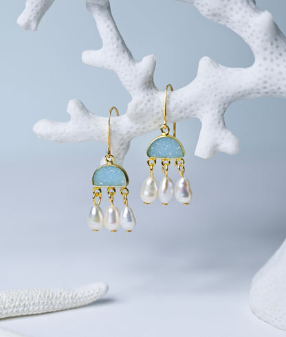 Close up view of blue chalcedony and pearl chandelier earrings hanging from a coral branch.