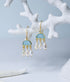 Close up view of blue chalcedony and pearl chandelier earrings hanging from a coral branch.
