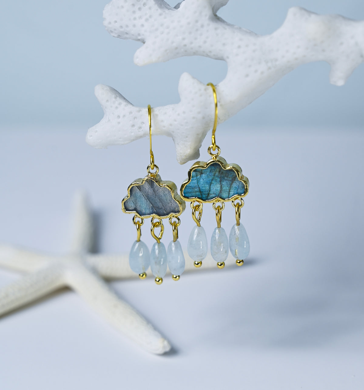 Close up view of labradorite and aquamarine chandelier earrings hanging from a white coral branch.