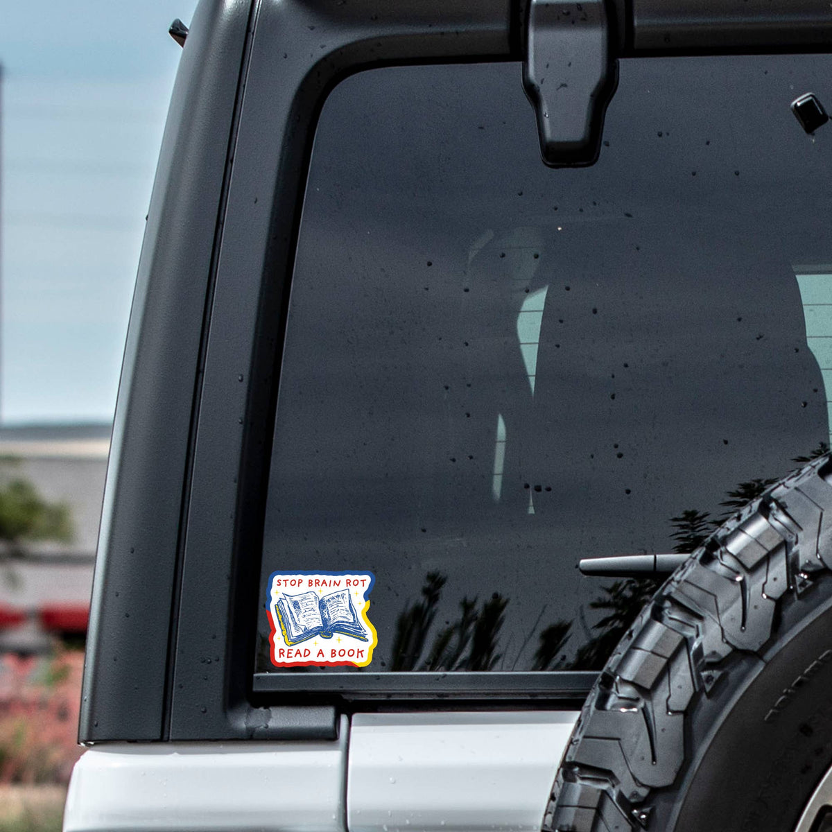 Car window with a sticker and a tire visible outdoors