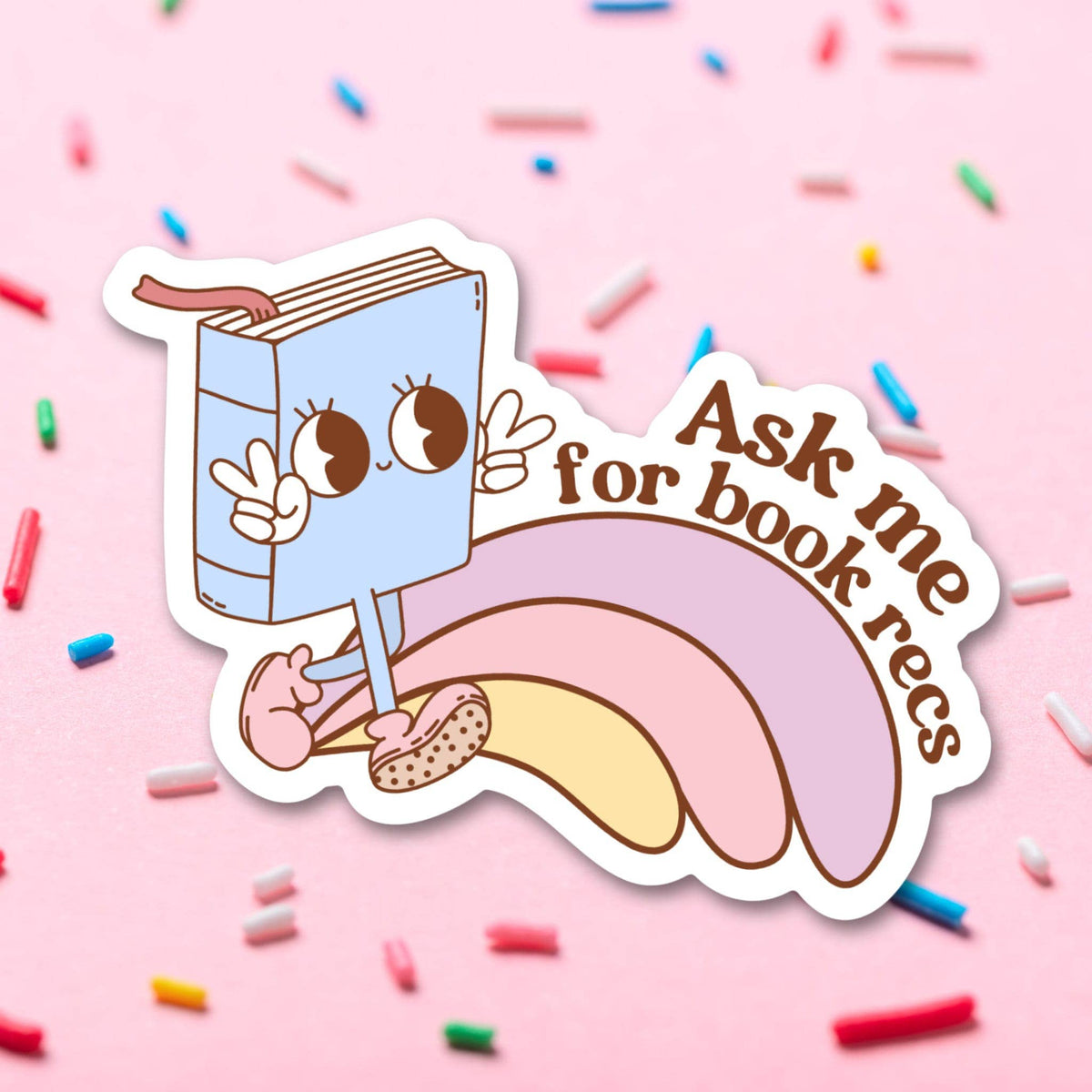Sticker with a cartoon book character on a pink background with sprinkles.