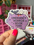 A hand with bright pink nail polish holds a die-cut sticker shaped like a purple pig. The sticker has black text reading &