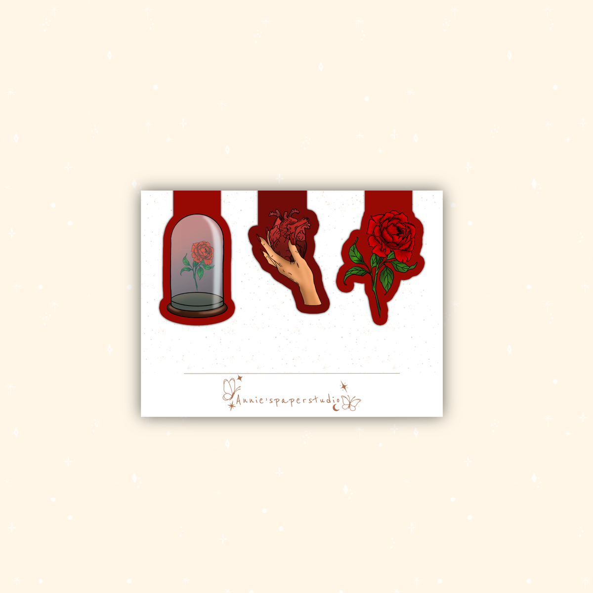 A white rectangular art print or card centered on a warm beige background, featuring three red-themed illustrations: a rose under a glass cloche, a hand holding a red heart, and a red rose with green leaves. A small cursive signature is printed near the bottom.