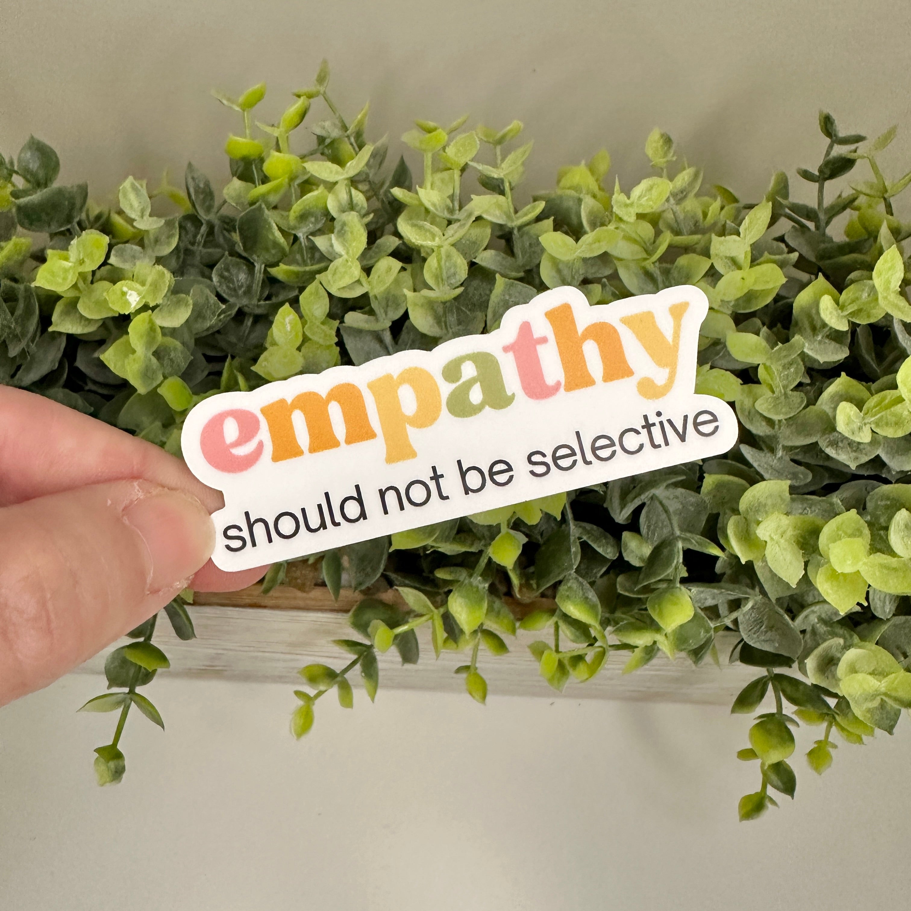 Hand holding a pro-empathy sticker text in front of plant