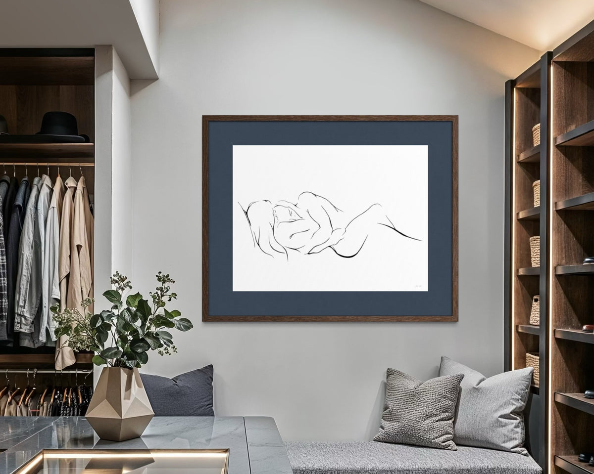 An elegant and classy minimalist line art print on a white background depicting two intertwined figures, embracing one another and finding peace and love. Large 30x40" print matted in deep blue with oak frame on wall in walk-in closet.