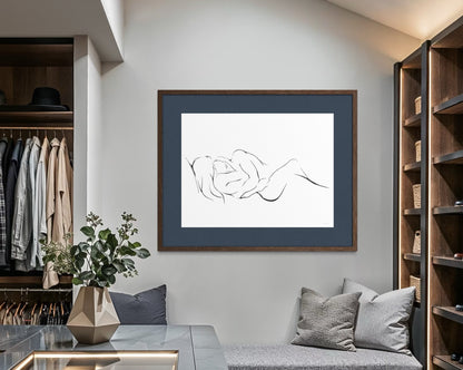 An elegant and classy minimalist line art print on a white background depicting two intertwined figures, embracing one another and finding peace and love. Large 30x40" print matted in deep blue with oak frame on wall in walk-in closet.