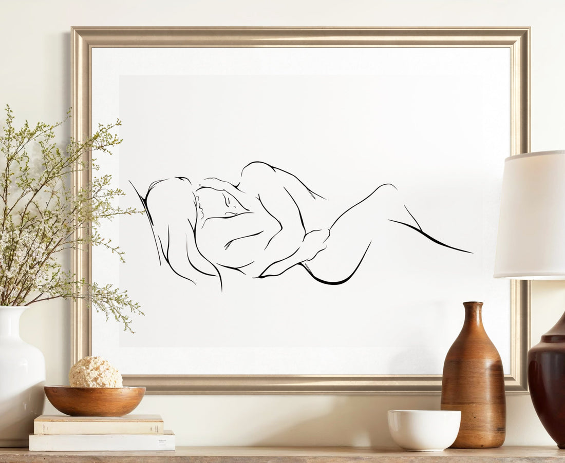An elegant and classy minimalist line art print on a white background depicting two intertwined figures, embracing one another and finding peace and love. in a brushed gold frame hung over a rustic wooden console table.