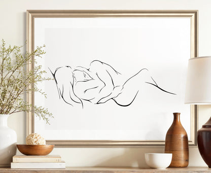 An elegant and classy minimalist line art print on a white background depicting two intertwined figures, embracing one another and finding peace and love. in a brushed gold frame hung over a rustic wooden console table.