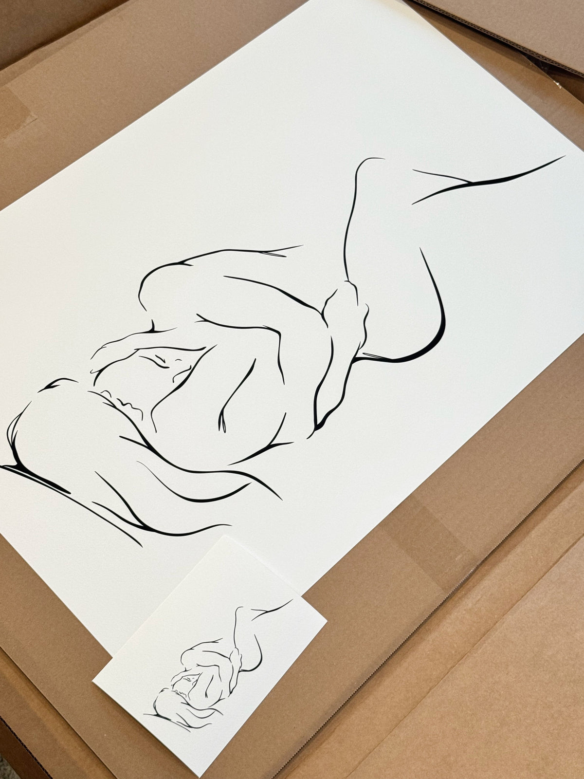 A minimalist line art print of two intertwined figures, one embracing the other, a large 30x40" print shown next to a smaller 5x7" of the same artwork.
