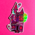 A die-cut sticker featuring a stylized haunted house with glowing neon green and silver ghosts, shown on a textured hot pink background.