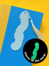 Glowing blue worm-shaped bookmark with tassel on a yellow background