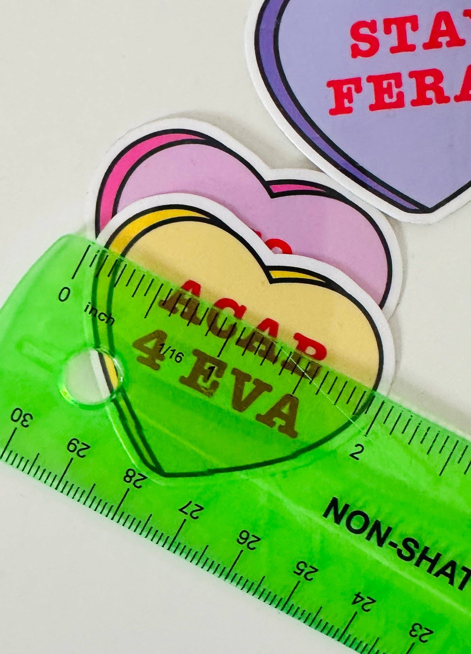 Colorful heart-shaped stickers with text and a green ruler on a white background