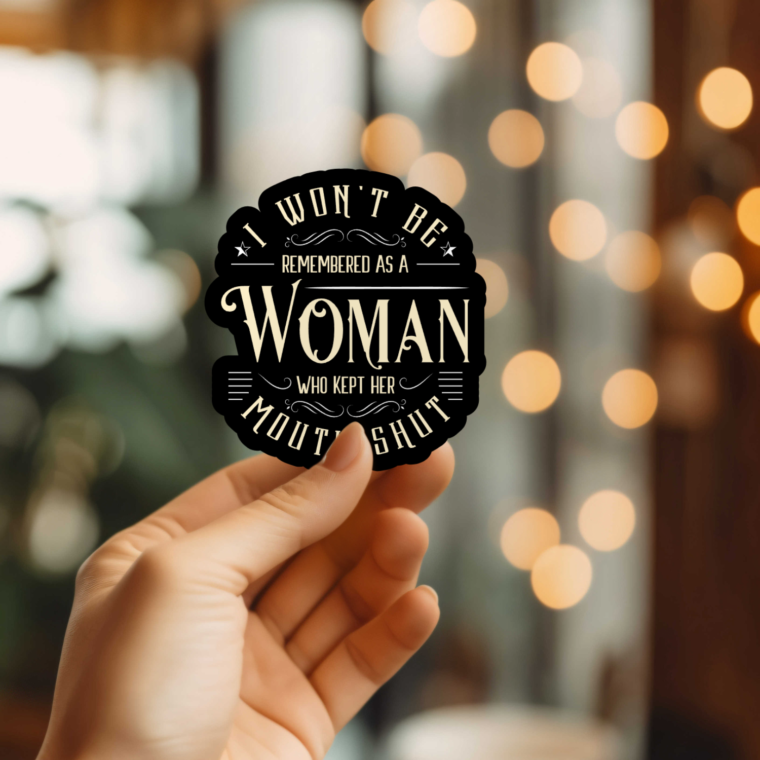 Hand holding a black sticker with white text against a blurred bokeh background
