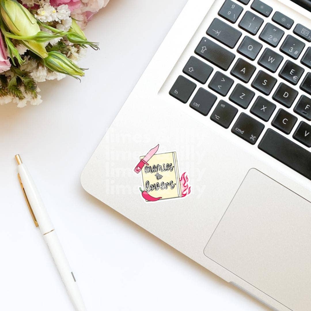 Laptop with a sticker on a white surface next to flowers and a pen