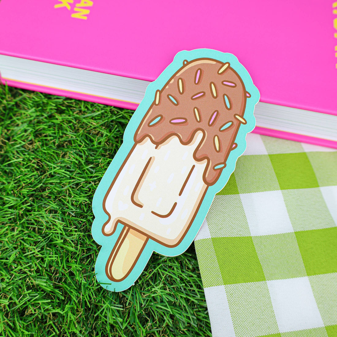 Ice cream stick-shaped bookmark on grass with a pink book in the background