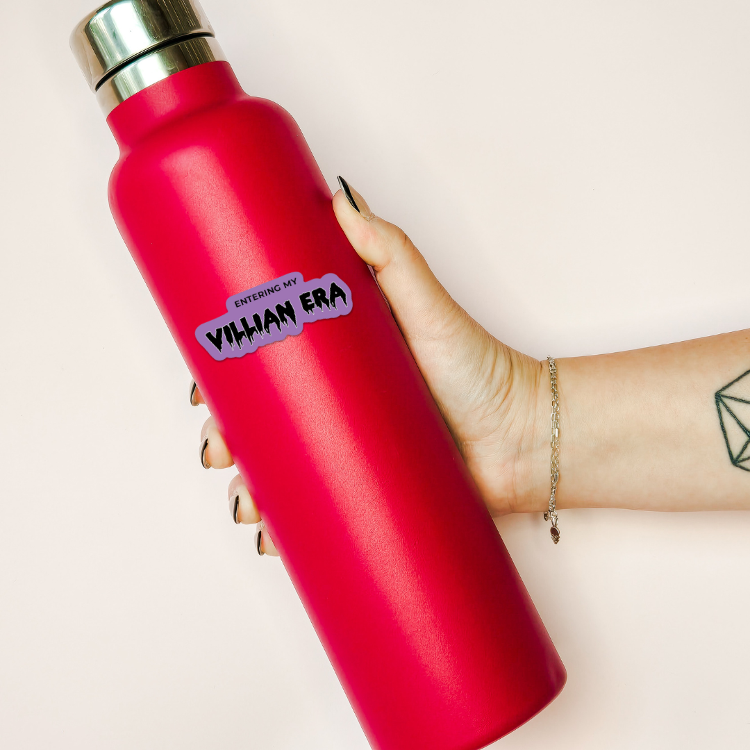 Red water bottle with a purple sticker held by a hand on a light background