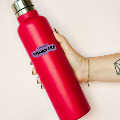 Red water bottle with a purple sticker held by a hand on a light background