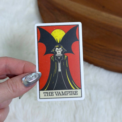 A hand with silver nail polish holds a tarot card featuring &