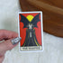 A hand with silver nail polish holds a tarot card featuring &