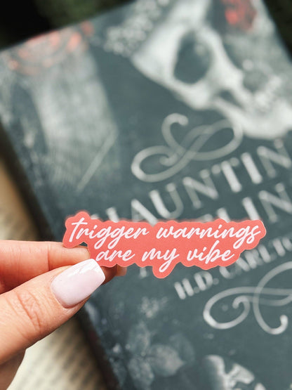 Hand holding a pink sticker with text in front of a book titled &