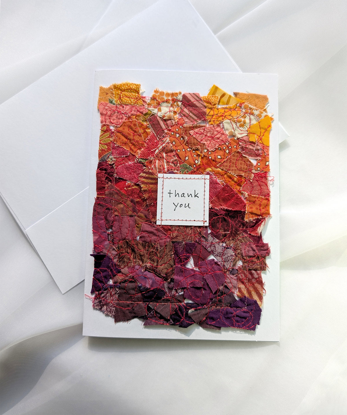 Orange and red fabric collage on a 5 by 7 blank white card with "thank you" handwritten on the front.