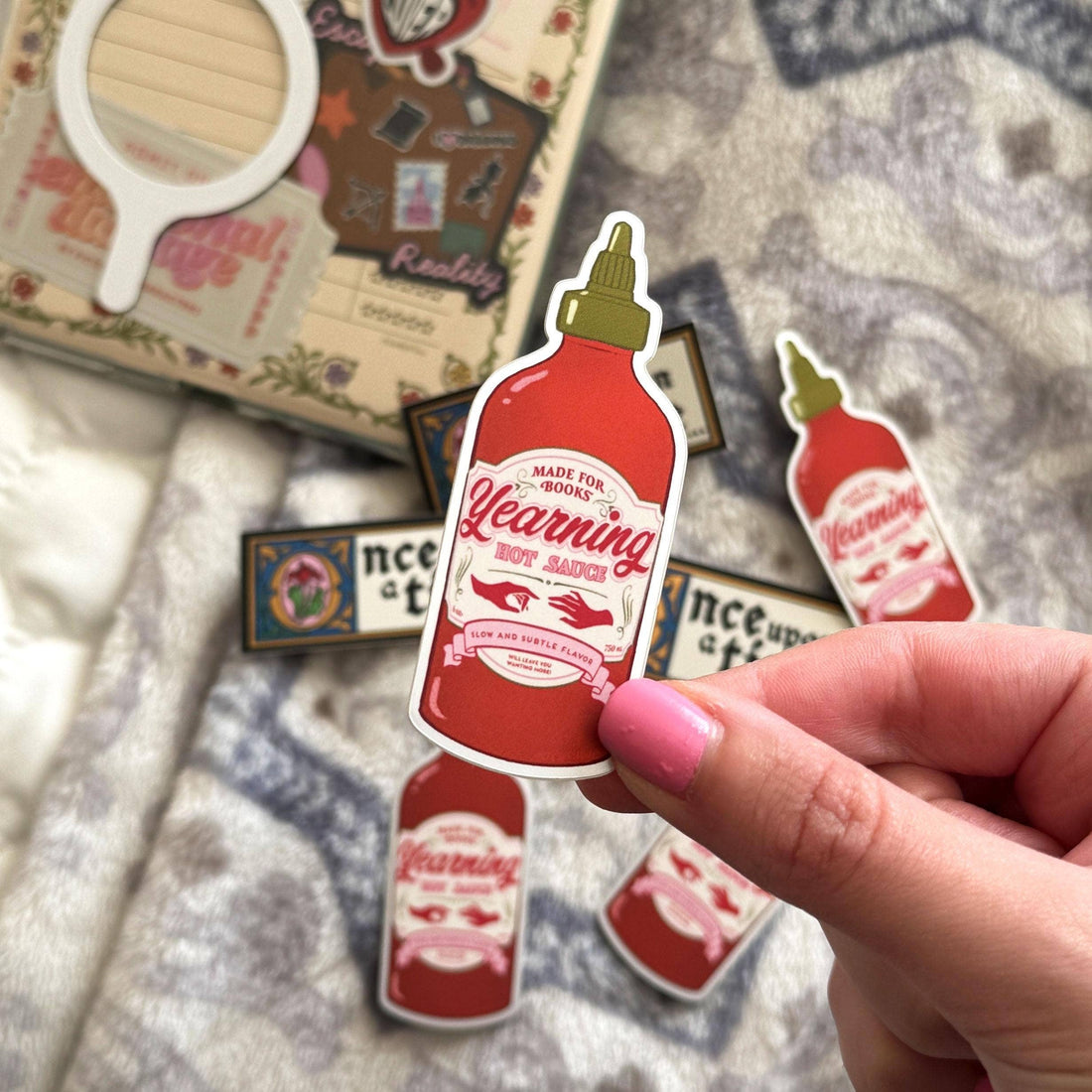 Sticker of a hot sauce bottle with a hand holding it, on a textured surface.