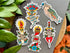 Colorful tattoo-style stickers on a gray surface with green leaves and orange flowers in the background.