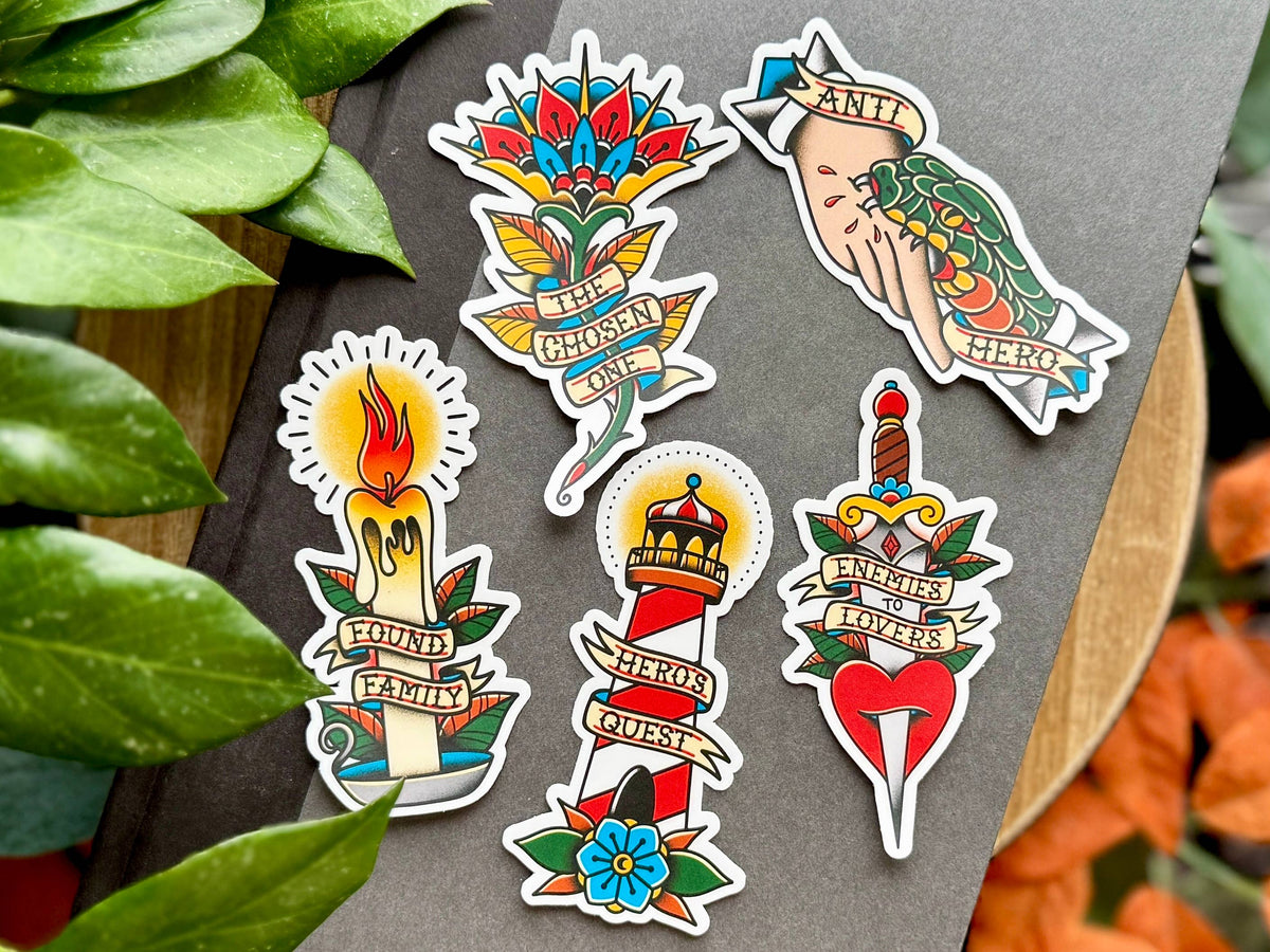 Colorful tattoo-style stickers on a gray surface with green leaves and orange flowers in the background.